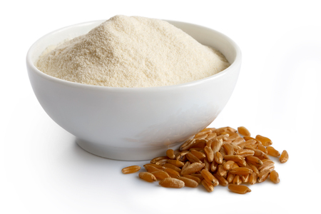 White flour
 in white ceramic bowl isolated on white. Next to kamut wheat kernels.の写真素材