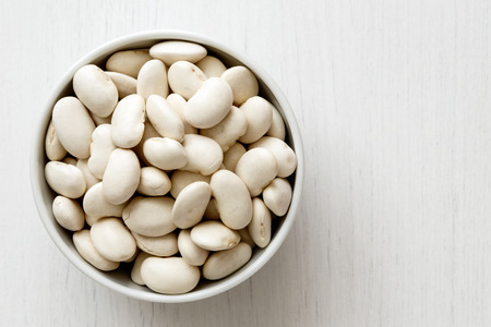 Dry butter beans
 in white ceramic bowl isolated on painted white wood from above.の写真素材