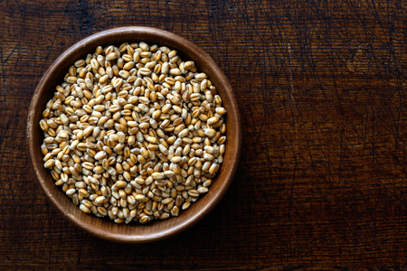 Winter wheat kernels in dark wooden bowl isolated on dark brown wood from above.の写真素材