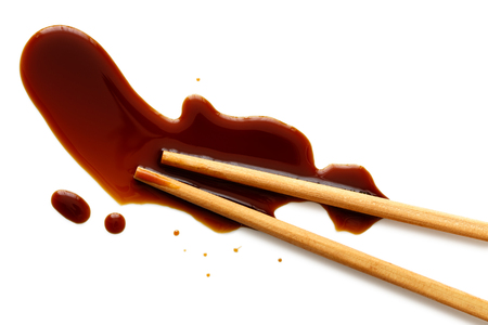 Spilled soya sauce on white with wooden chopsticks from above.の写真素材