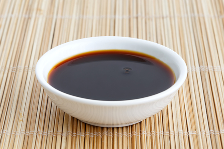 Soya sauce in white ceramic bowl isolated on bamboo mat.の写真素材