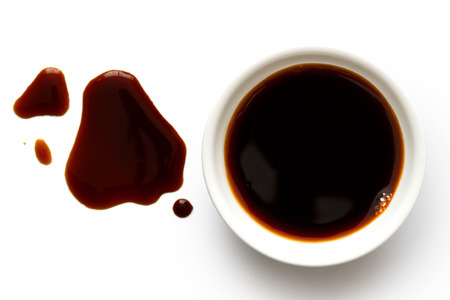 Soya sauce in white ceramic bowl isolated on white from above. Spilled soya sauce.