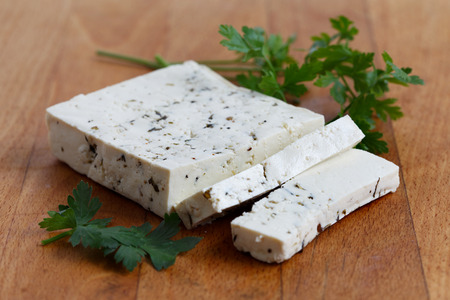 Block of natural tofu with herbs, two tofu slices and fresh parsley  on wooden chopping board.