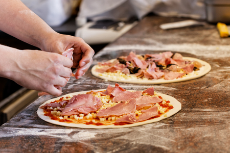 Cook putting toppings on two pizzas.の写真素材