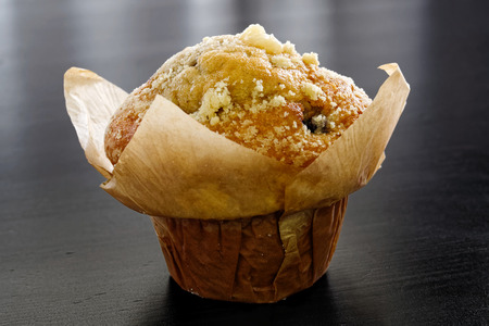 Whole baked blueburry muffin in baking paper cup isolated on black wooden table.の写真素材