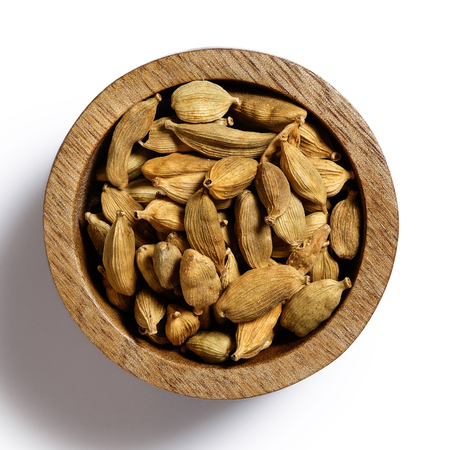 Dry cardamom pods in dark wood bowl isolated on white from above.の写真素材