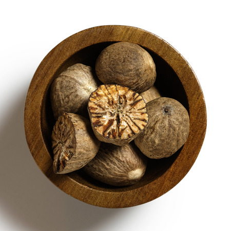 Dried whole and cut nutmegs in dark wood bowl isolated on white from above.の写真素材