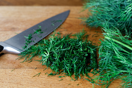 Freshly chopped up bunch of dill on wood chopping board next to kitchen knife.の写真素材