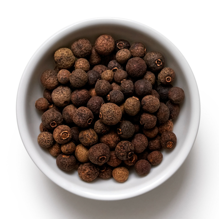 Whole allspice in white ceramic bowl isolated on white from above.