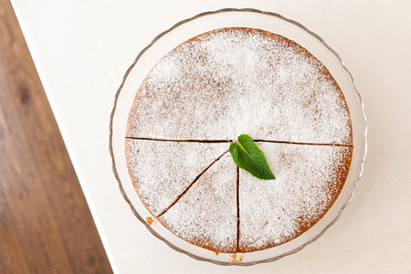 Whole cut sponge cake with icing sugar on glass stand isolated on white table from above. Mint leaf...