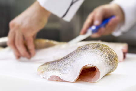 A large zander fish fillet lying on a white chopping board. A chef filleting a fish in the...
