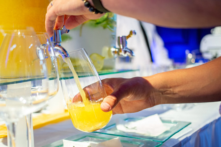 Glass being filled with orange juice from glass drinks dispenser at social event.の写真素材