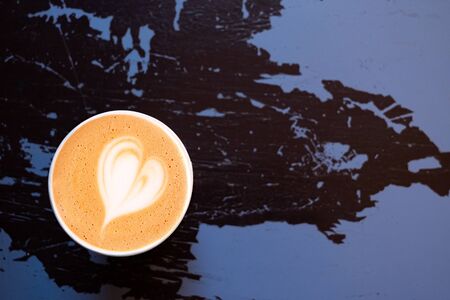 Cappuccino in a paper take away cup isolated on peeling and cracked black and purple painted wood...