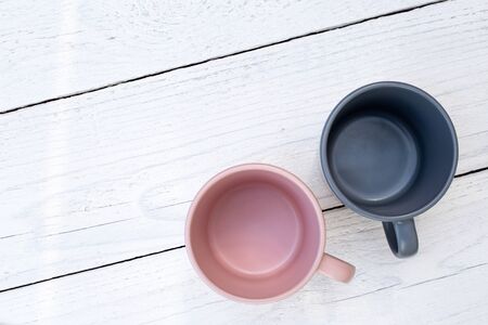 Two empty ceramic mugs, pink and blue-grey, isolated on white painted wood from above. Space for text.の写真素材