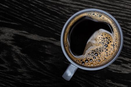 Black coffee in a blue-grey ceramic mug isolated on dark brown wood table with grain from above. Space for text.の写真素材