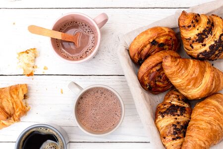 Continental breakfast with hot chocolate, black coffee and basket of pastries. Half eaten on white wood from above.の写真素材