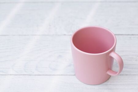 Empty pink ceramic mug isolated on white painted wood. Space for text.の写真素材
