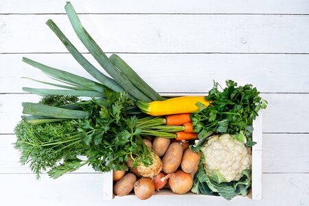 Wooden box of fresh vegetables from farmers market on white painted wood table from above. Space for text.の写真素材