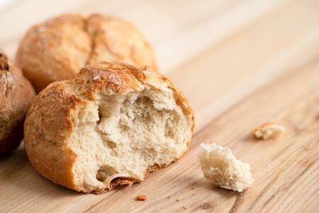 Broken round rustic white bread roll next to two round bread rolls on light wood.の写真素材
