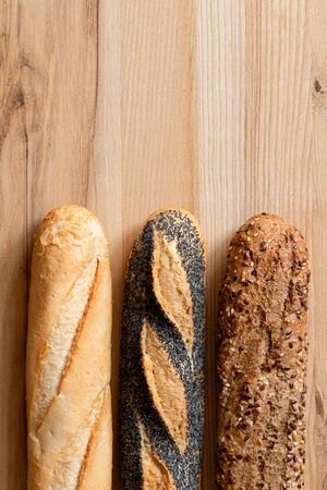 Three traditional baguettes on light wood. Plain, whole wheat and poppy seed. Top view. Space for text.の写真素材