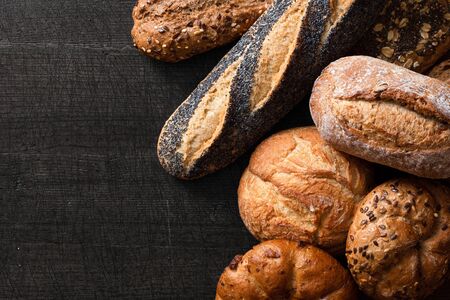 Mixed baguettes and bread rolls on dark grey wood. Top view. Space for text.の写真素材