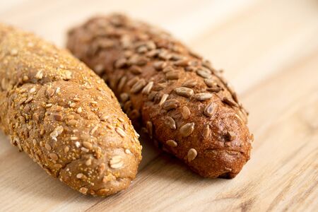 Long whole wheat sunflower seed bread roll and long whole wheat sesame seed bread roll on light wood.の写真素材