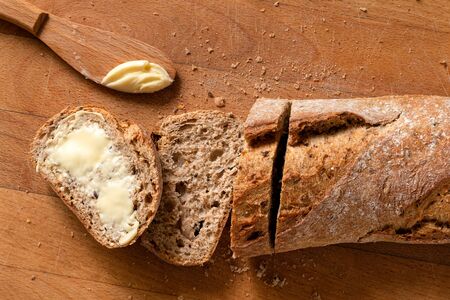 Sliced loaf of whole wheat european bread on light wood. Buttered slice. Top view.の写真素材