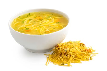 Instant chicken noodle soup in a white ceramic bowl next to a pile of dry instant soup isolated on white.の写真素材