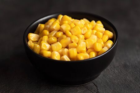 Canned sweet corn in a black ceramic bowl isolated on black slate.の写真素材