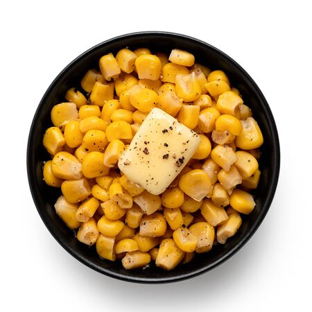 Canned sweet corn with a knob of butter and ground black pepper in a black ceramic bowl isolated on white. Top view.の写真素材