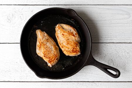 Two whole chicken breasts roasting in cast iron pan isolated on white. Top view.の写真素材
