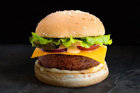 Plant based burger in sesame bun with salad and cheese isolated on black slate.の写真素材