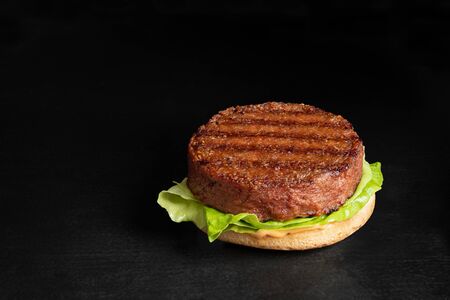 Freshly grilled plant based burger patty on bun with lettuce and sauce isolated on black surface. Copy space.の写真素材