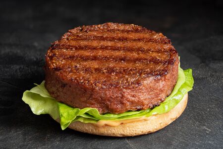 Freshly grilled plant based burger patty on bun with lettuce and sauce isolated on black slate.の写真素材