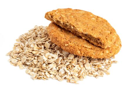 One and half crunchy oat and wholemeal biscuits on a heap of oats isolated on white.の写真素材