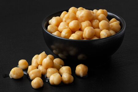 Cooked chick peas in a black ceramic bowl isolated on black painted wood. Spilled chick peas.の写真素材