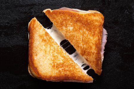 Classic cheese and ham toasted sandwich cut in half isolated on black cast iron griddle. Top view.