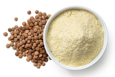 Dried lentil flour in a white ceramic bowl next to a pile of brown lentils isolated on white. Top view.の写真素材