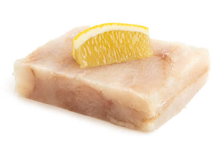 Quick frozen fish fillet block with a lemon wedge isolated on white.の写真素材