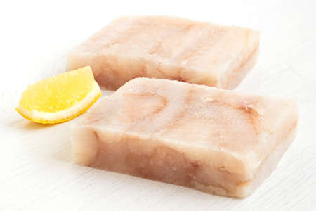 Two quick frozen pollock fillet blocks with a lemon wedge isolated on white.