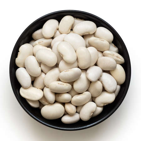 White beans in a black ceramic bowl isolated on white. Top view.の写真素材