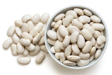 White beans in a white ceramic bowl next to a pile of white beans isolated on white. Top view.の写真素材