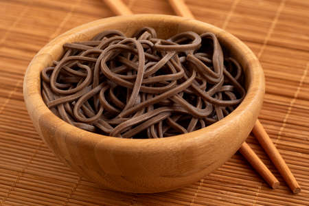 Cooked soba noodles in a bamboo bowl on a bamboo matt next to chop sticks.の写真素材