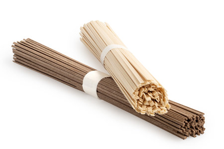 A bundle of dry udon noodles on top of a bundle of dry soba noodles isolated on white.の写真素材