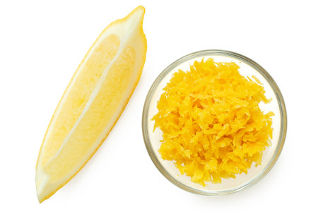 Freshly grated lemon zest in a glass bowl next to lemon segment isolated on white. Top view.の写真素材