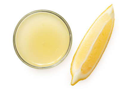 Freshly squeezed lemon juice in a glass bowl next to lemon segment isolated on white. Top view.の写真素材