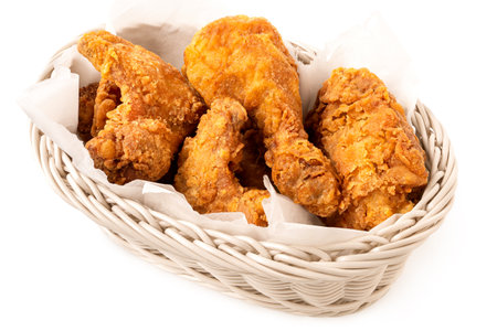 Crispy fried chicken pieces in a white woven basket isolated on white.の写真素材