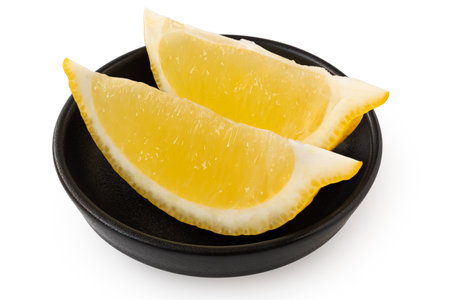 Two segments of fresh lemon in black ceramic dish isolated on white.の写真素材