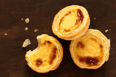Three portuguese custard egg tarts with crumbs on dark wood background. Top view.の写真素材
