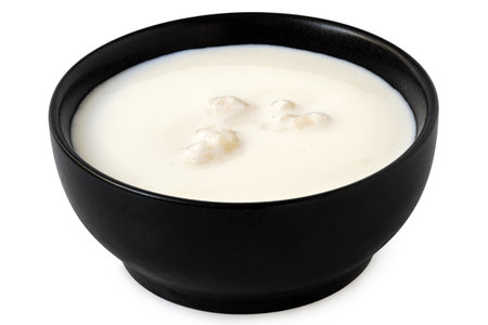 Milk with kefir grains in a black ceramic bowl isolated on white.の写真素材
